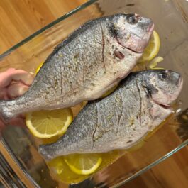 Dorada (sea bream) in a baking dish with lemon, wine, olive oil, and garlic.