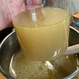 The Ultimate Homemade Chicken Stock in a measuring cup is Rich, Flavorful, and Nutritious