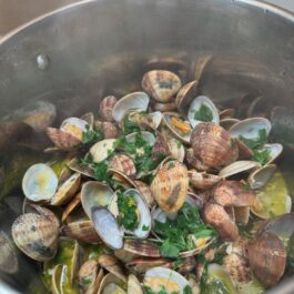 Adding cilantro to steamed clams in garlic cilantro white wine sauce; Portuguese Bulhao Pato