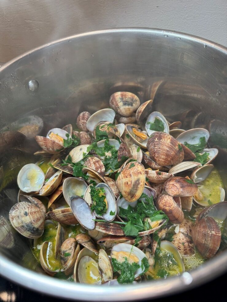 Adding cilantro to steamed clams in garlic cilantro white wine sauce; Portuguese Bulhao Pato