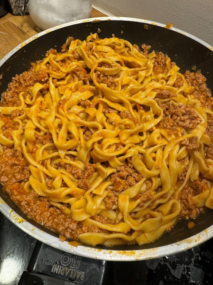 Tagliatelle al Bolognese in the pan combining the sauce with the pasta